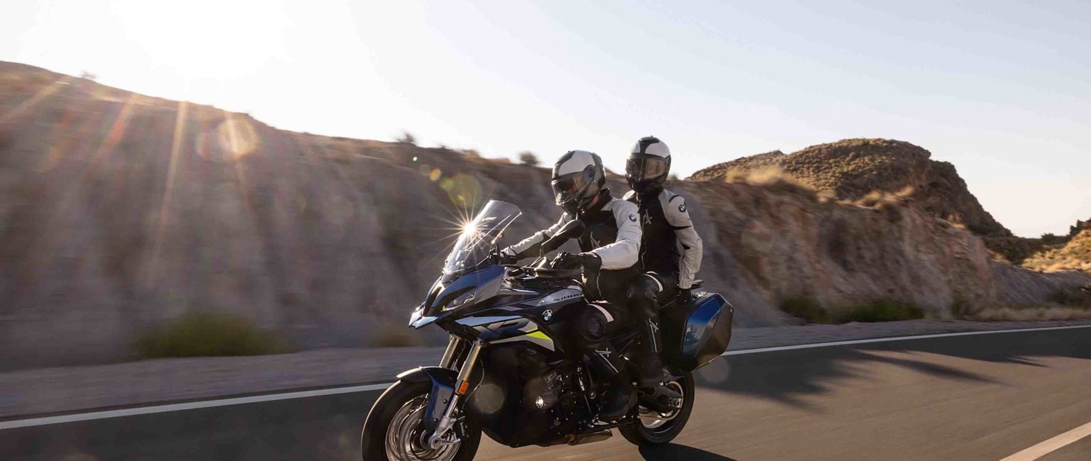 Två människor åker på en BMW-motorcykel bland höga berg