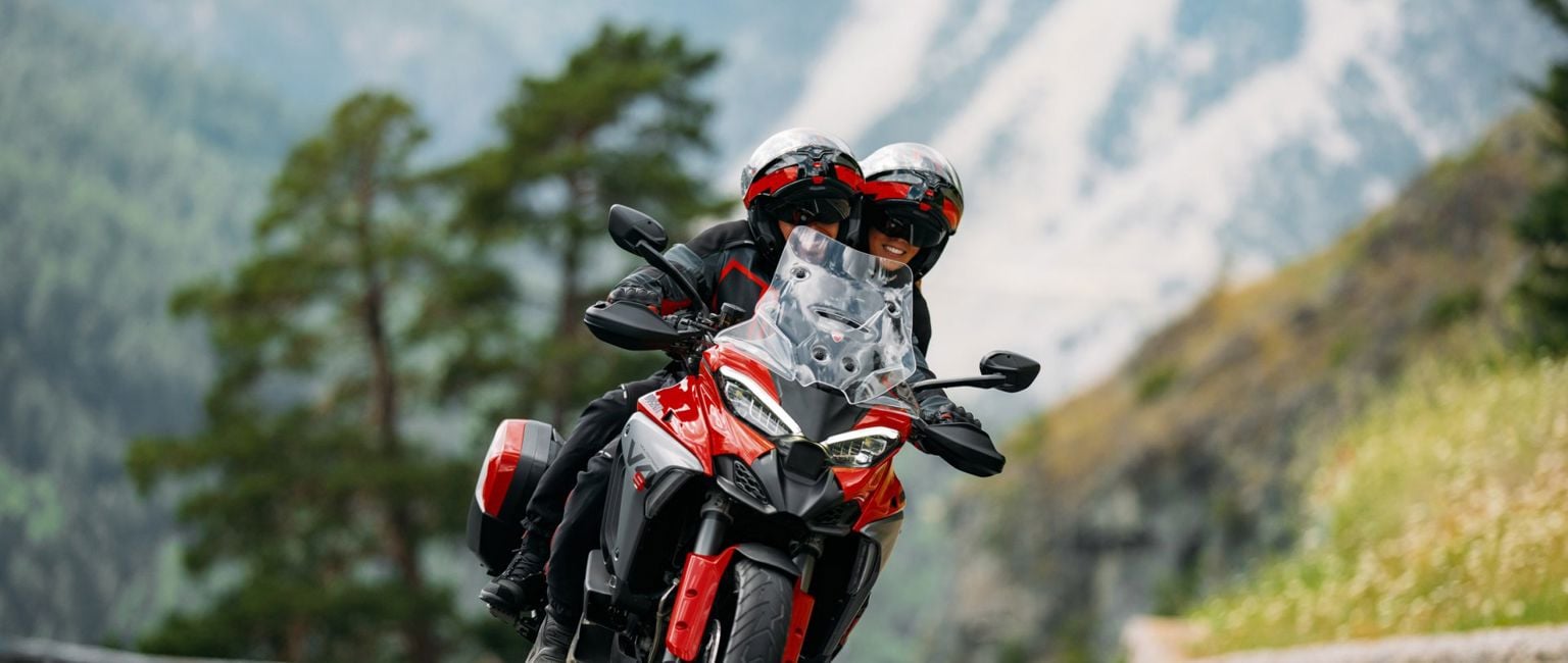 Två människor åker på en röd ducati-motorcykel på en landsväg