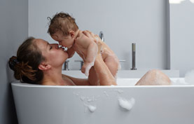 Bebis som badar badkar med sin mamma