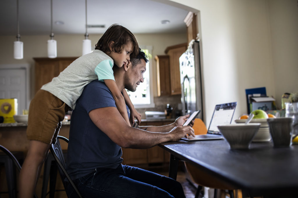 Pappa och son sitter vid matbordet och tittar ner i både telefon och dator och ser bekymrade ut