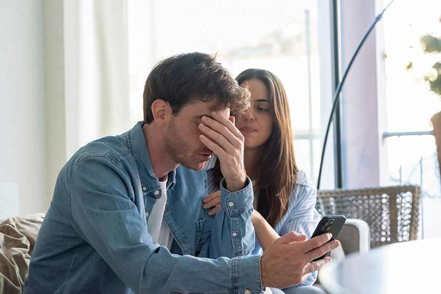 Man och kvinna sitter i en soffa och titta förtvivlat på en mobiltelefon