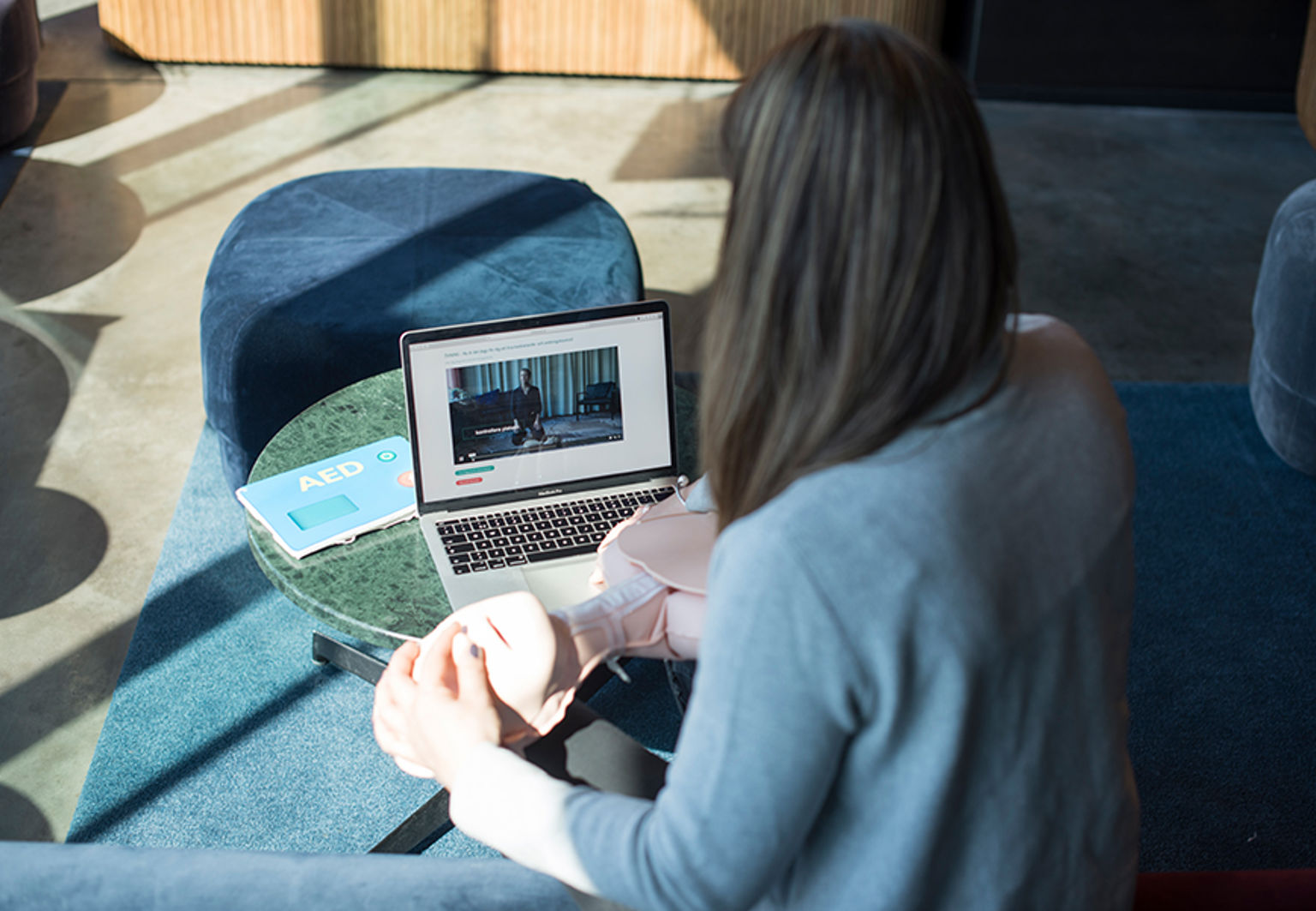 Kvinna håller i en HLR-docka och kollar på en instruktionsfilm på en laptop