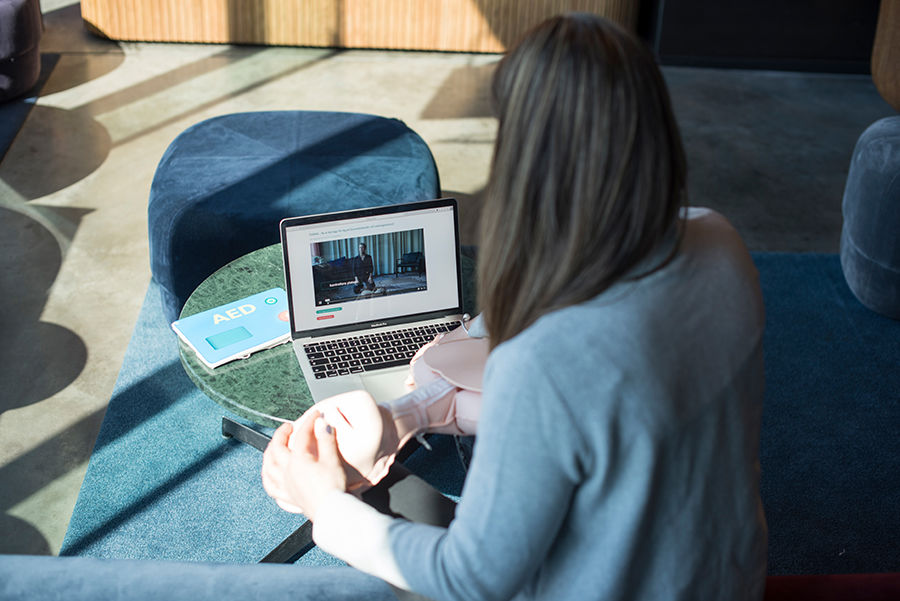 Kvinna håller i en HLR-docka och kollar på en instruktionsfilm på en laptop