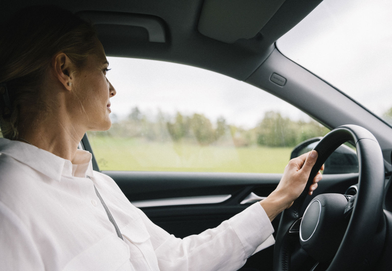 kvinna med vit skjorta på sig som kör bil