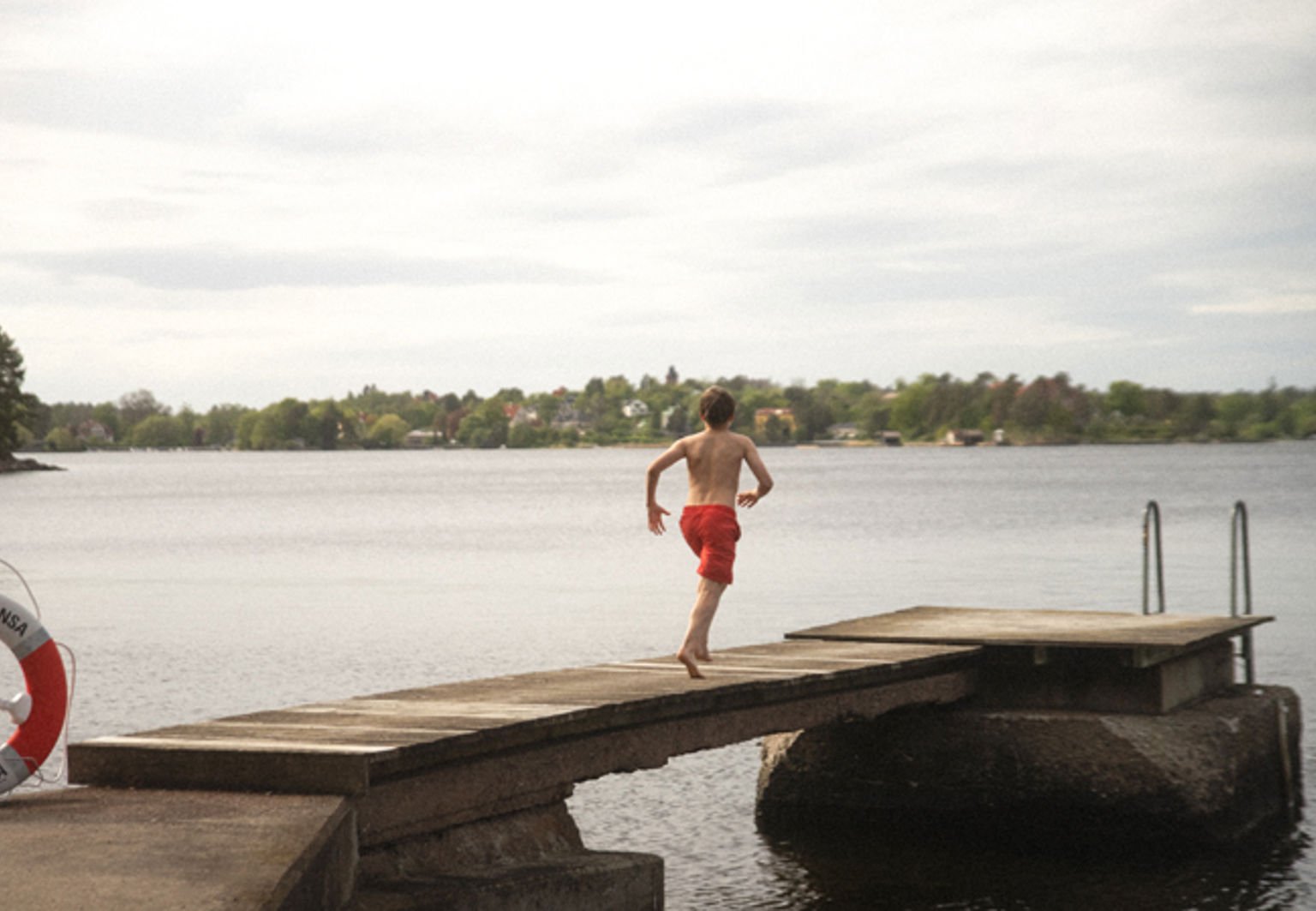 Pojke springer på en brygga en sommarkväll