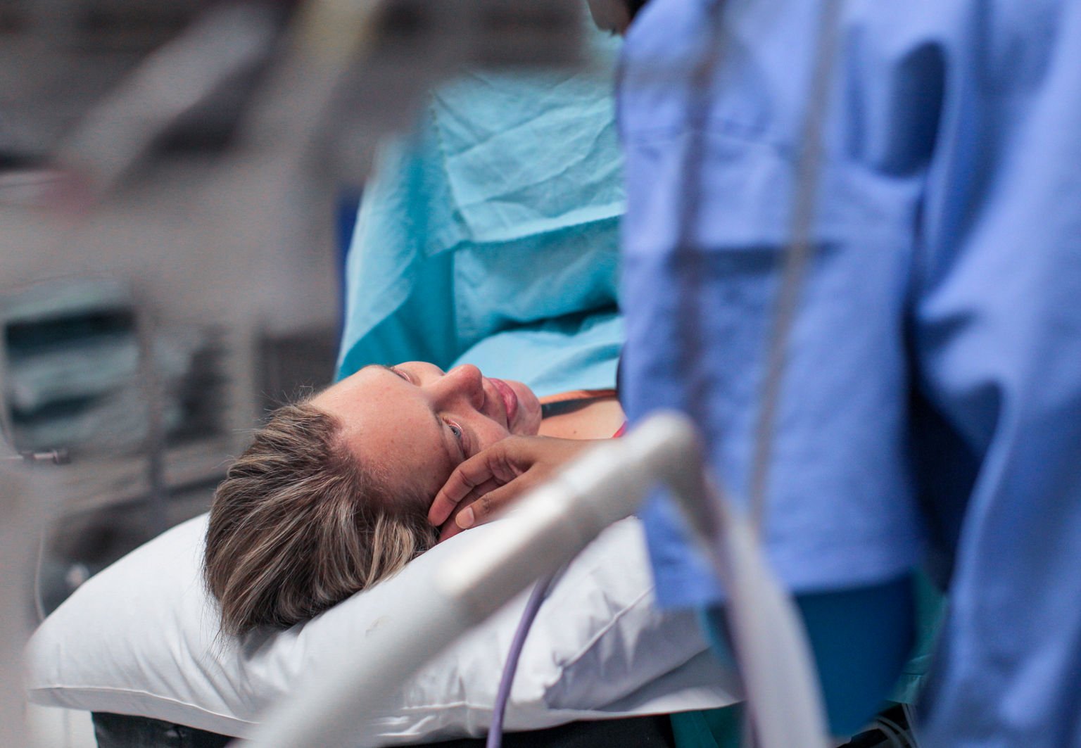 Kvinna ligger i operationssal och ska genomgå ett kejsarsnitt, hennes partner klappar henne på kinden