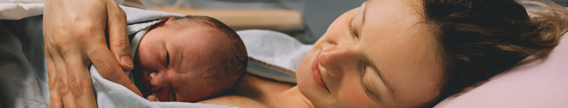 Bebis ligger på kvinnas bröst i förlossningsrum