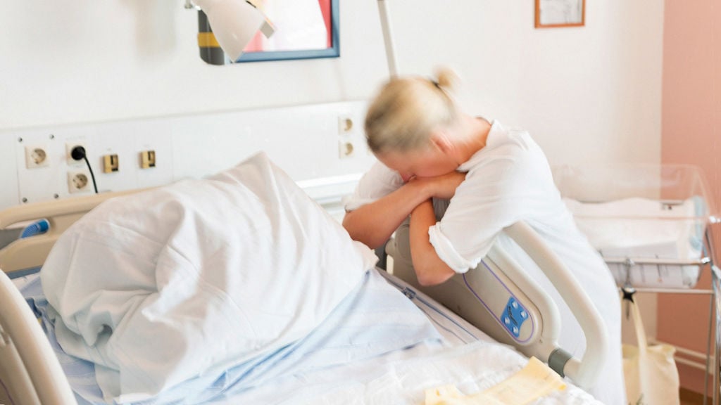 kvinna lutar sig mot en sjukhussäng