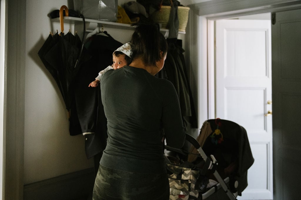 kvinna med sin bebis på axeln och barnvagn går ut genom en dörr