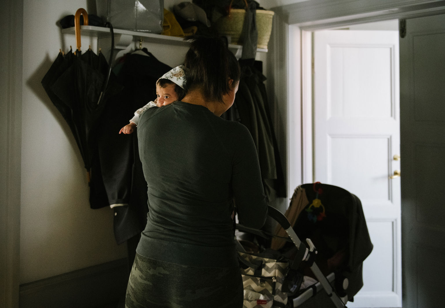 Kvinna bär på sin bebis och går ut med barnvagnen från sitt hus