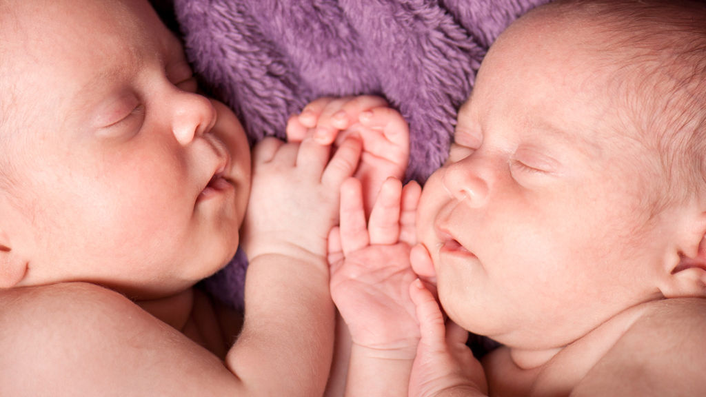 närbild på ett par tvillingar som sover på en lila filt