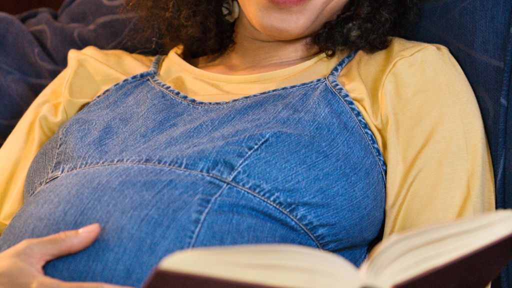 gravid kvinna i gul tröja och klänning ligger och läser