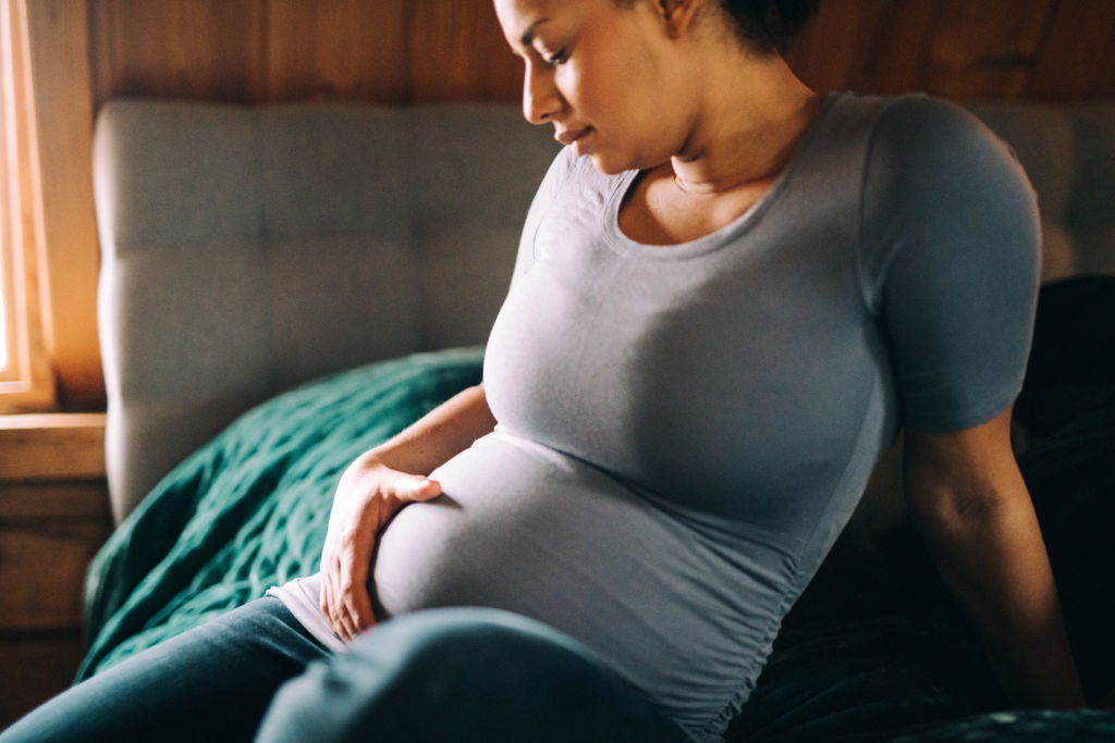Kvinna sitter på sängkanten och håller på sin gravida mage