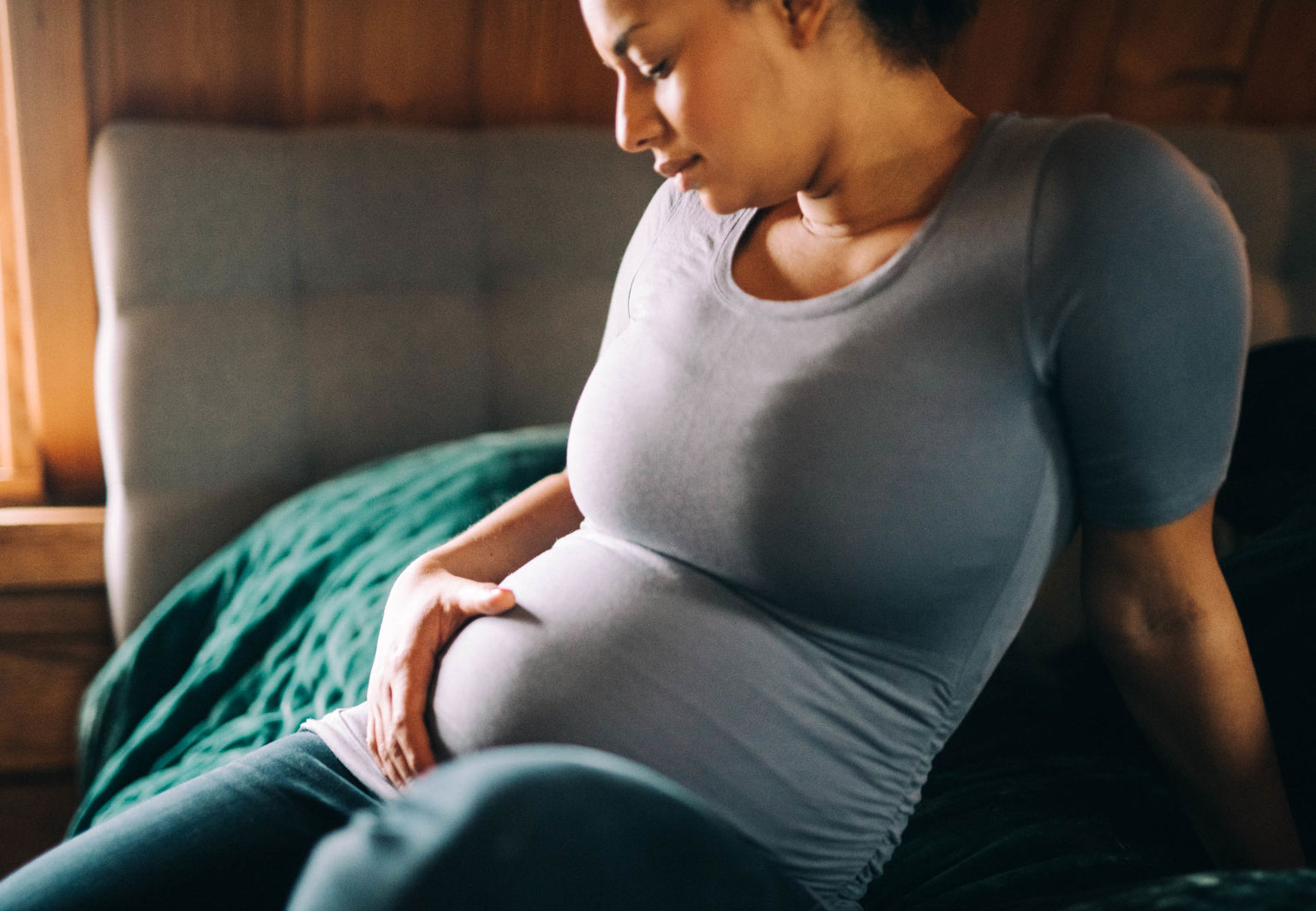 Kvinna sitter på sängkanten och håller en hand på sin gravida mage