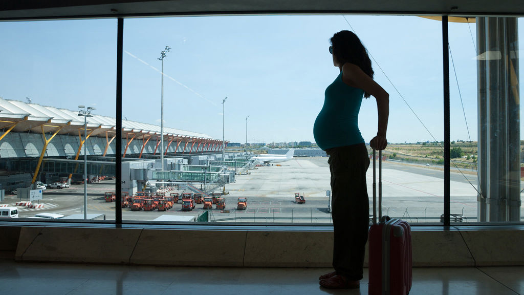 gravid kvinna står på en flygplats tittar ut mot gate