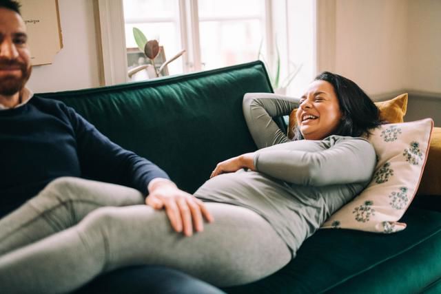 Gravid kvinna ligger i soffan och skrattar bredvid en man