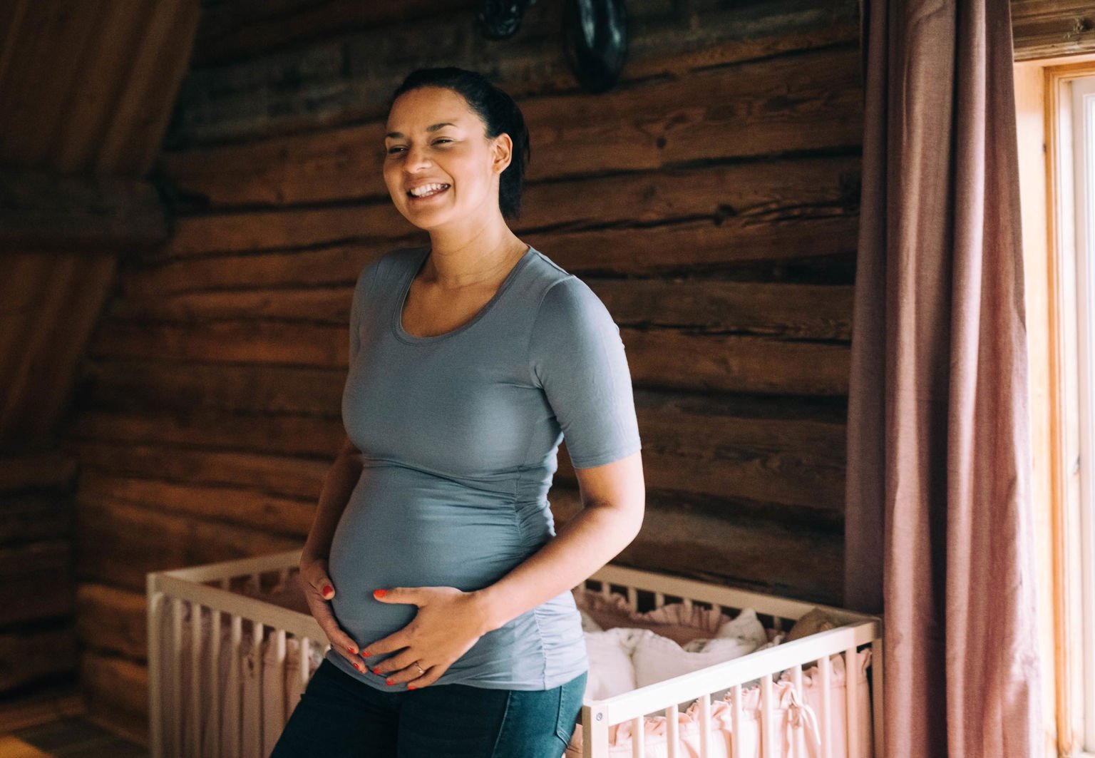 Kvinna står vid en spjälsäng och håller om sin gravida mage