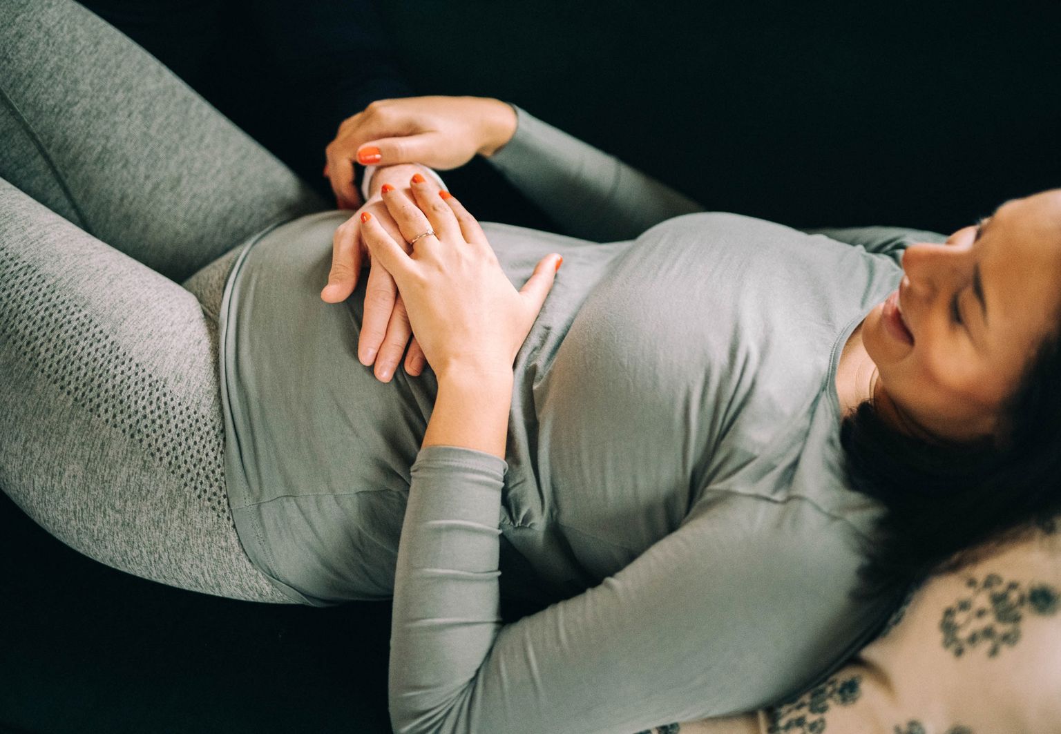 Kvinna ligger i soffan och låter sin partners hand känna på magen