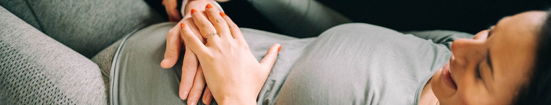 Kvinna ligger i soffan och låter sin partners hand känna på magen