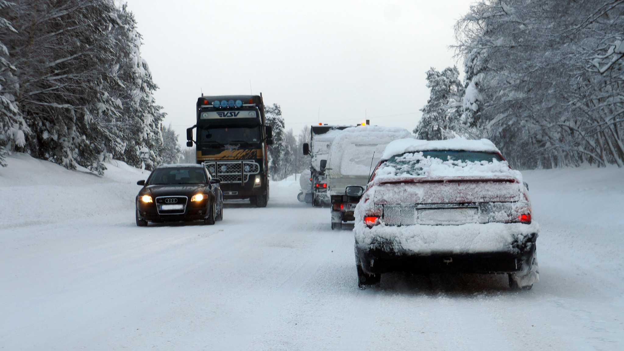 Snöiga bilar åker på en trafikerad väg på vinterväglag
