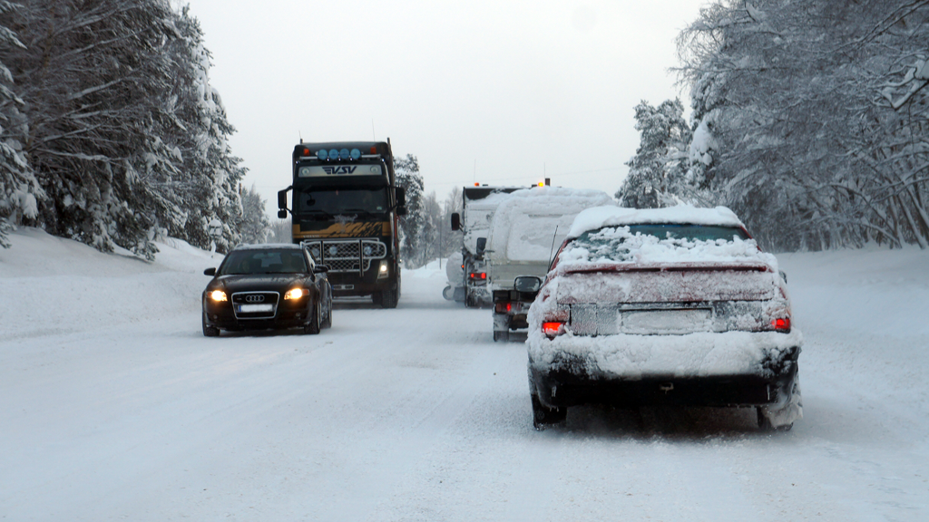 Snöiga bilar åker på en trafikerad väg på vinterväglag