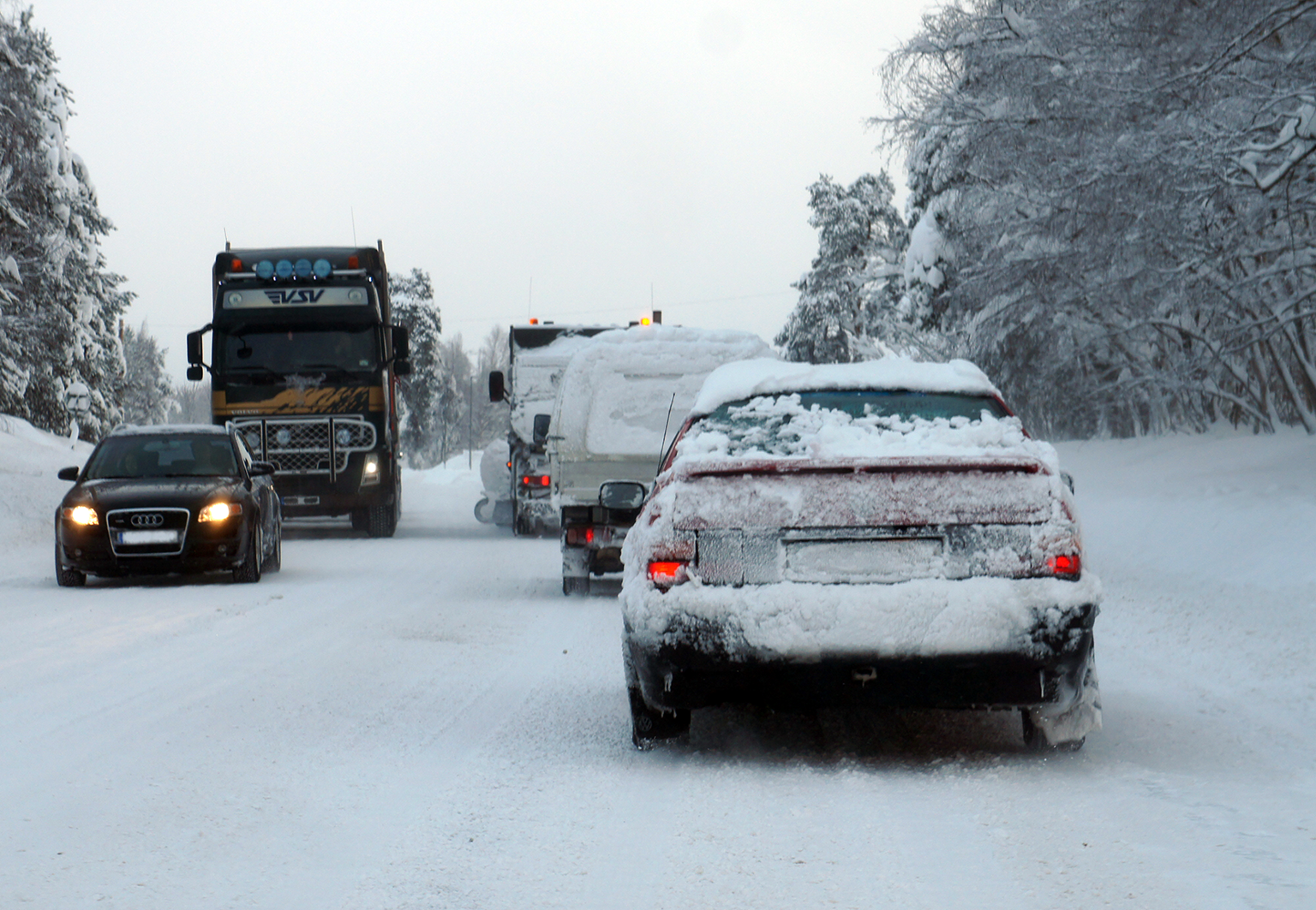 Snöiga bilar åker på en trafikerad väg på vinterväglag