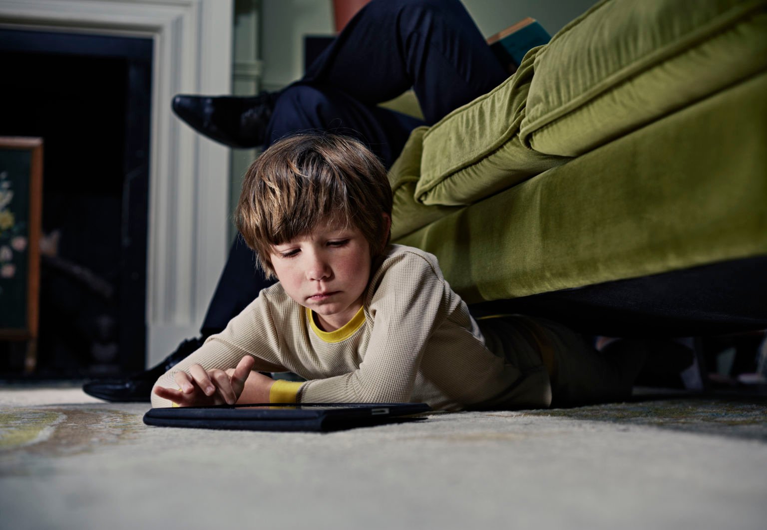 Pojke ligger under soffan och tittar på sin surfplatta
