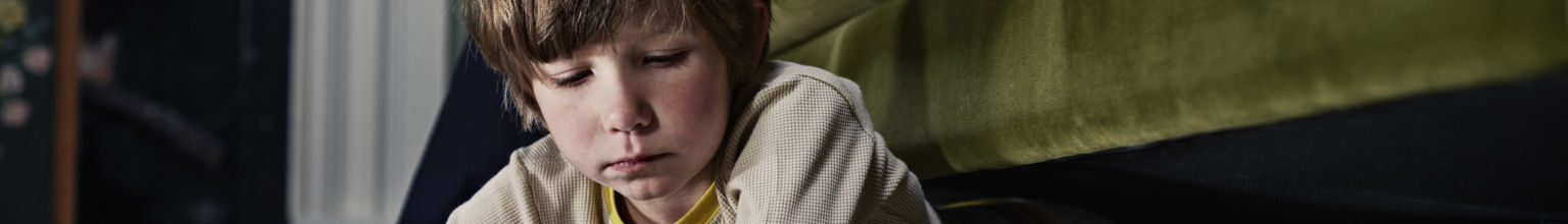 Pojke ligger under soffan och tittar på sin surfplatta