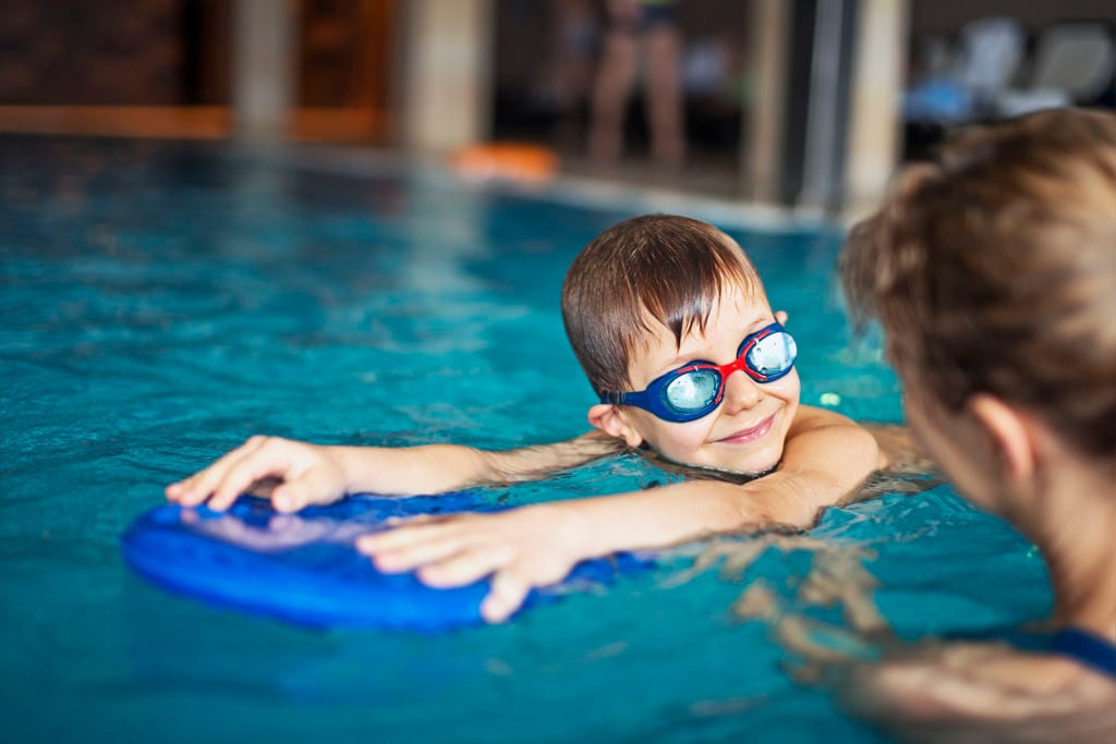 Pojke med simglasögon använder flytkudde i en pool