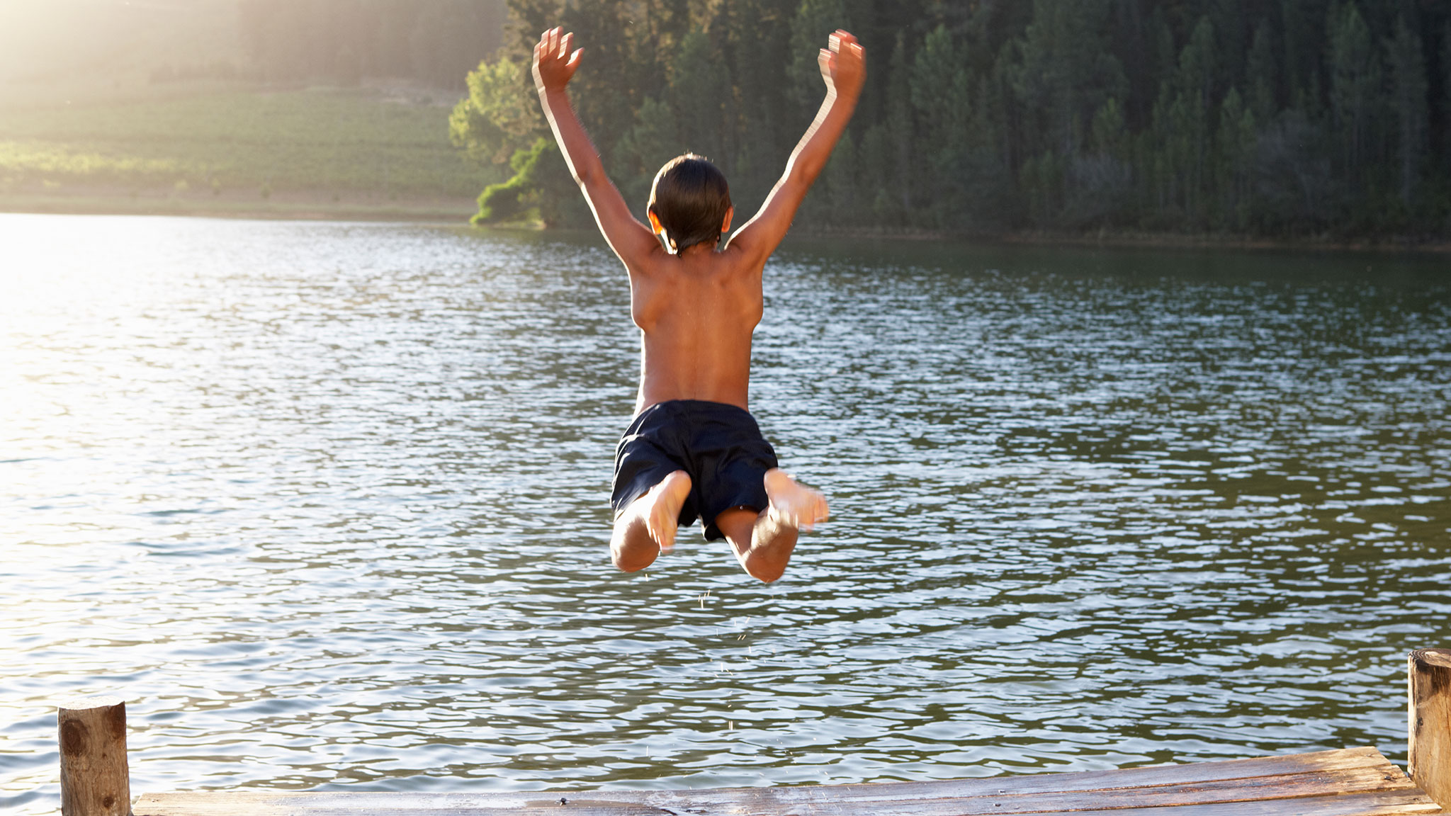 Pojke hoppar i vattnet från brygga