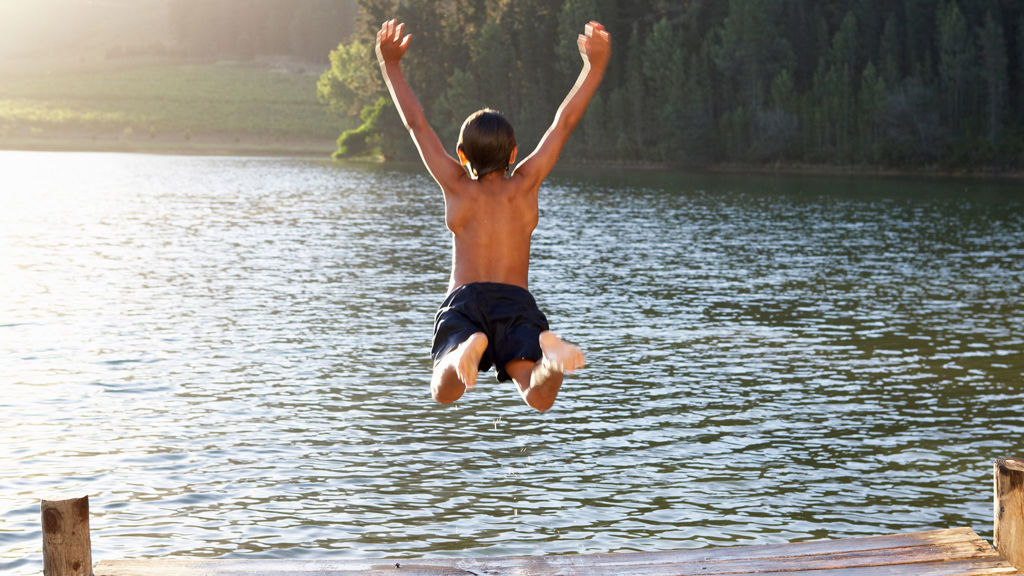 Pojke hoppar i vattnet från brygga