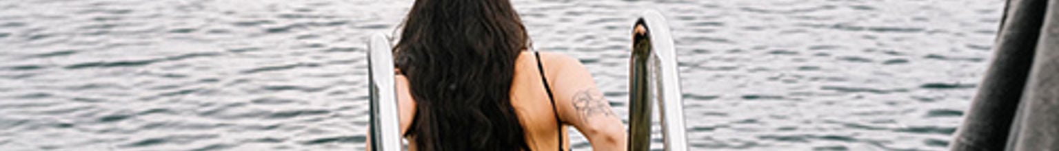 Kvinna med långt hår kliver ner i vatten på en stege