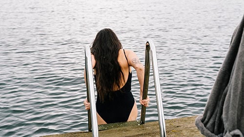 Kvinna med långt hår kliver ner i vatten på en stege
