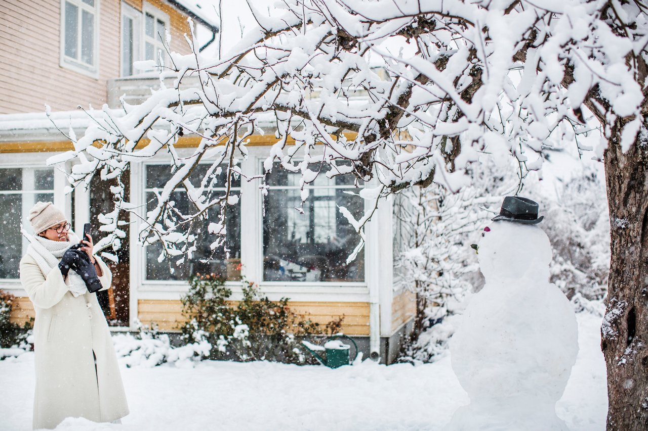 Kvinna fotar snögubbe på tomten
