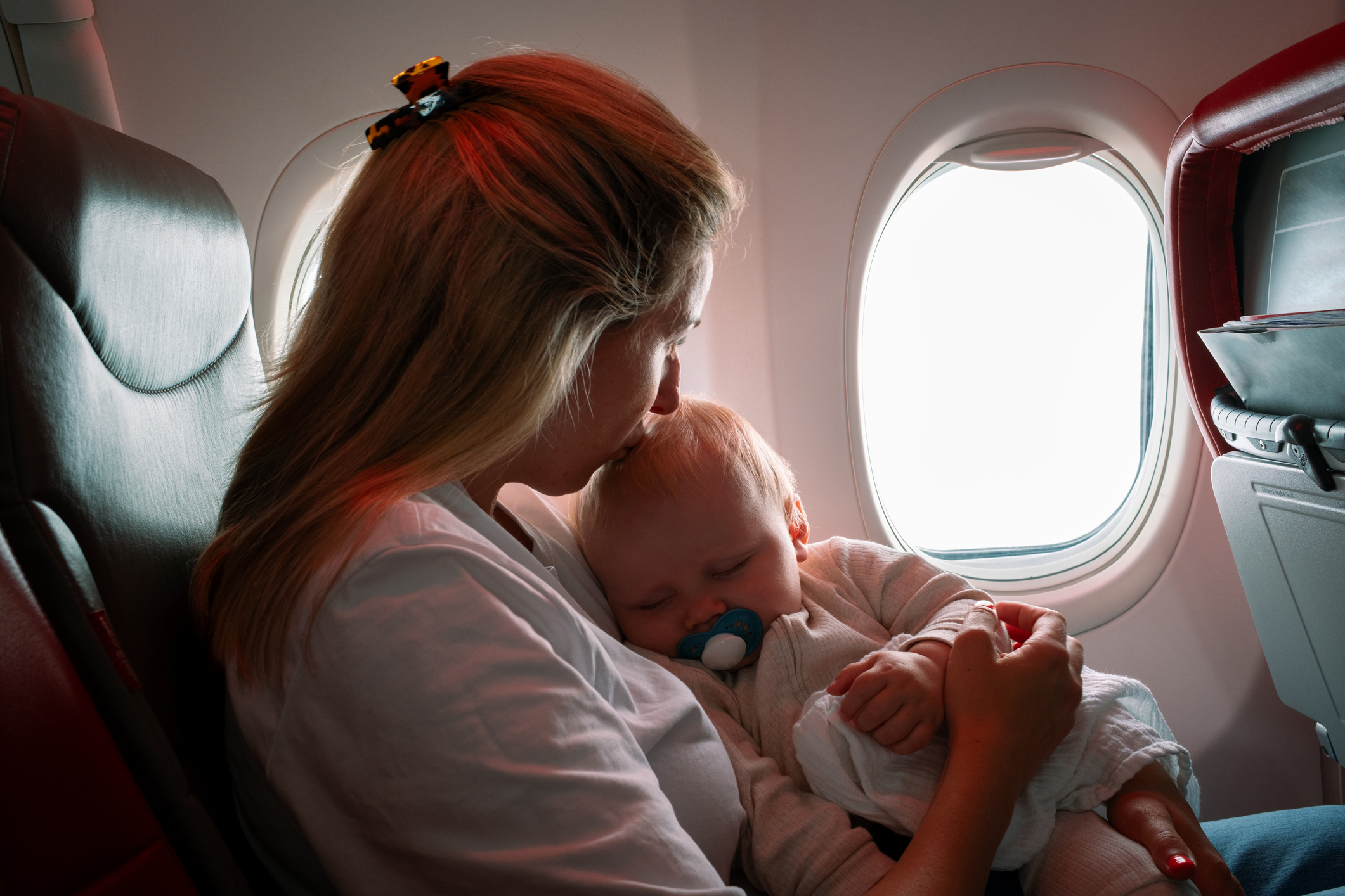 Mamma pussar en sovande bebis på pannan i ett flygplan