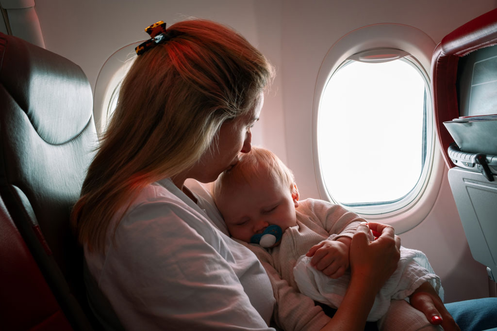 Mamma pussar en sovande bebis på pannan i ett flygplan