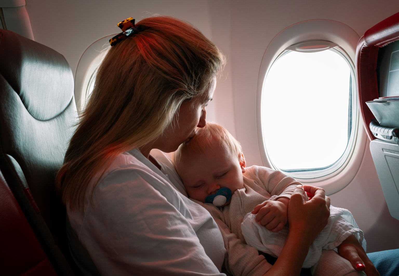 Mamma pussar en sovande bebis på pannan i ett flygplan