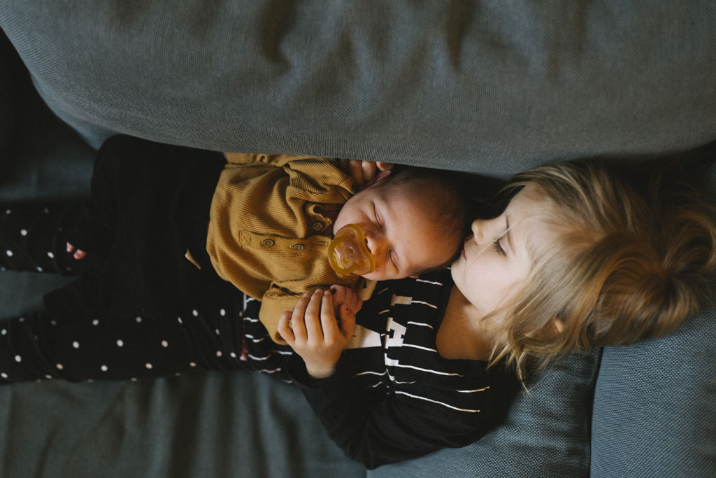 Storasyskon och bebis kramas i en soffa