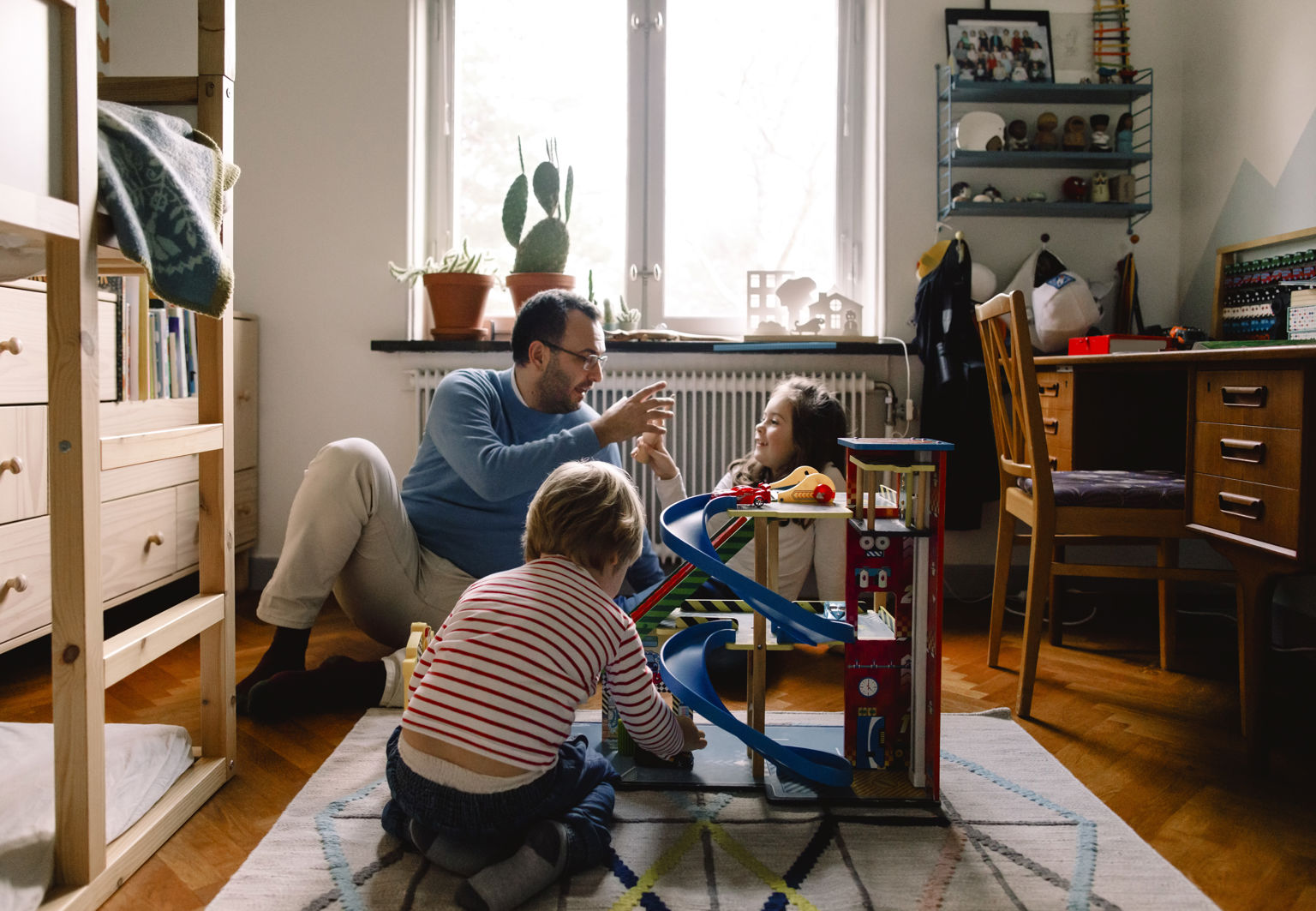 Pappa och två barn leker tillsammans med leksaker i ett barnrum