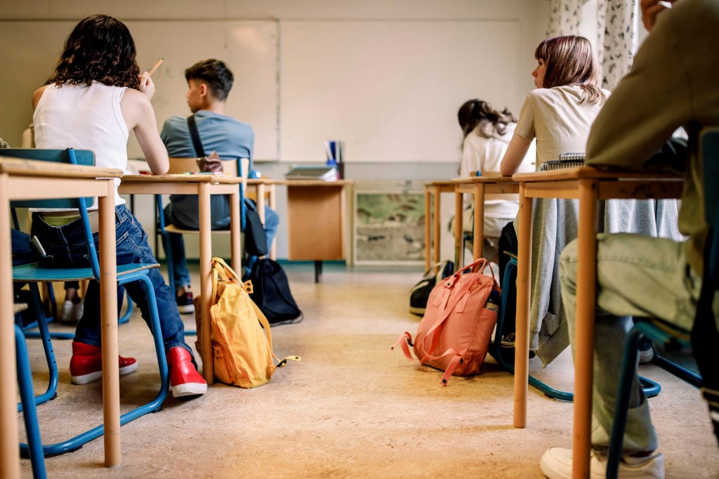 Flera ungdomar sitter i ett klassrum med tillhörande väskor på golvet