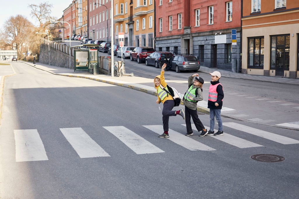 Tre glada barn med reflexväst går över ett övergångsställe