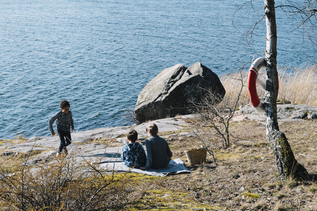 Tre pojkar leker och sitter vid vattnet vid klipporna