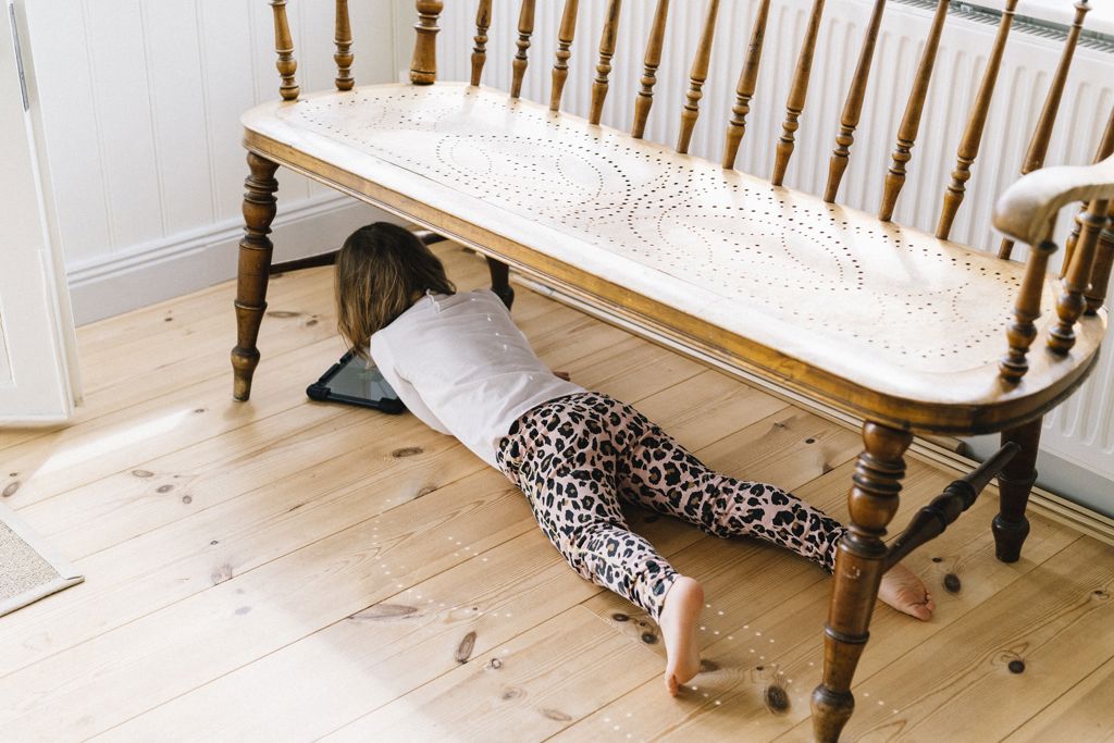 Barn spelar på sin surfplatta på golvet under en sittbänk inomhus