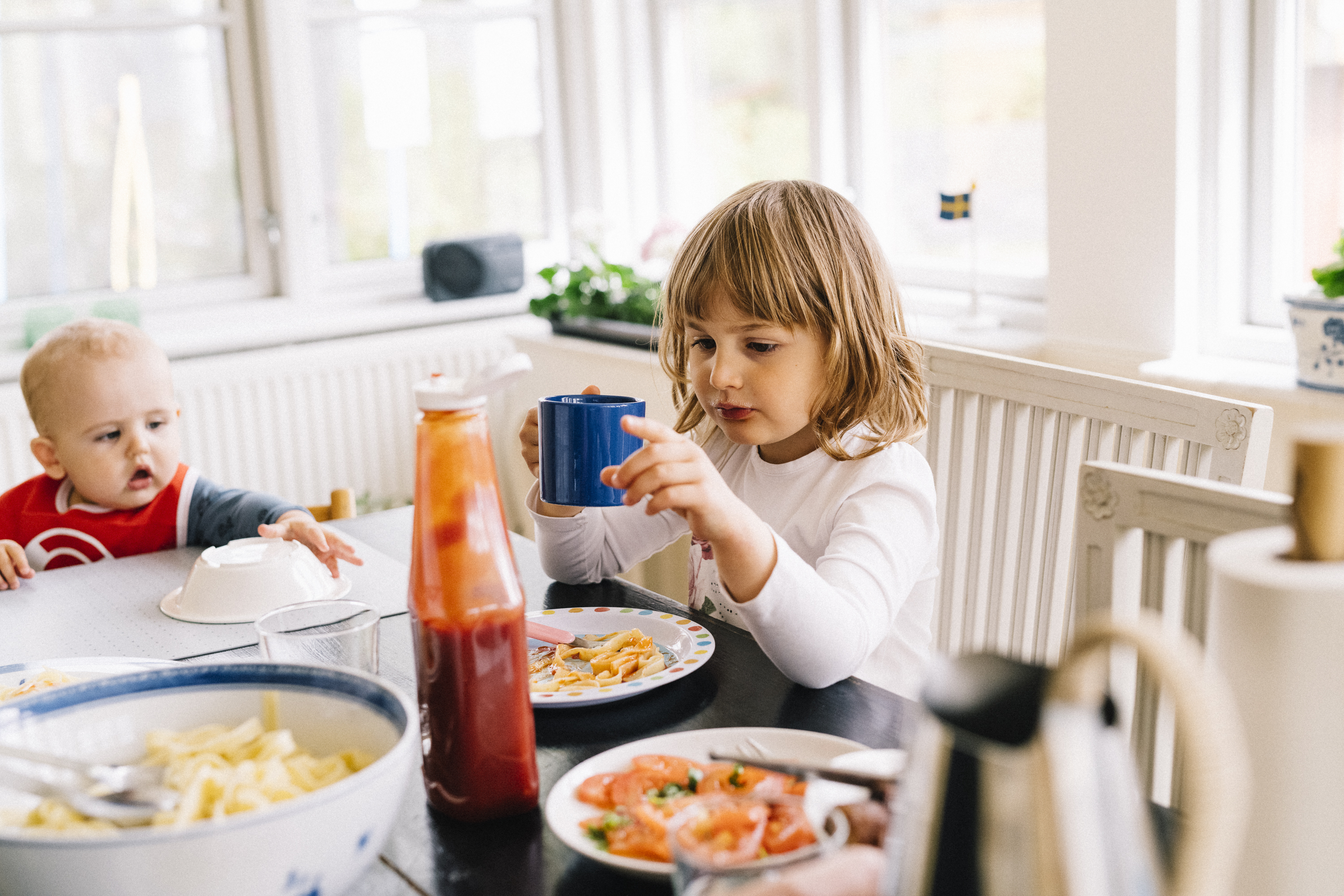 Två barn varav en bebis sitter vid ett matbord