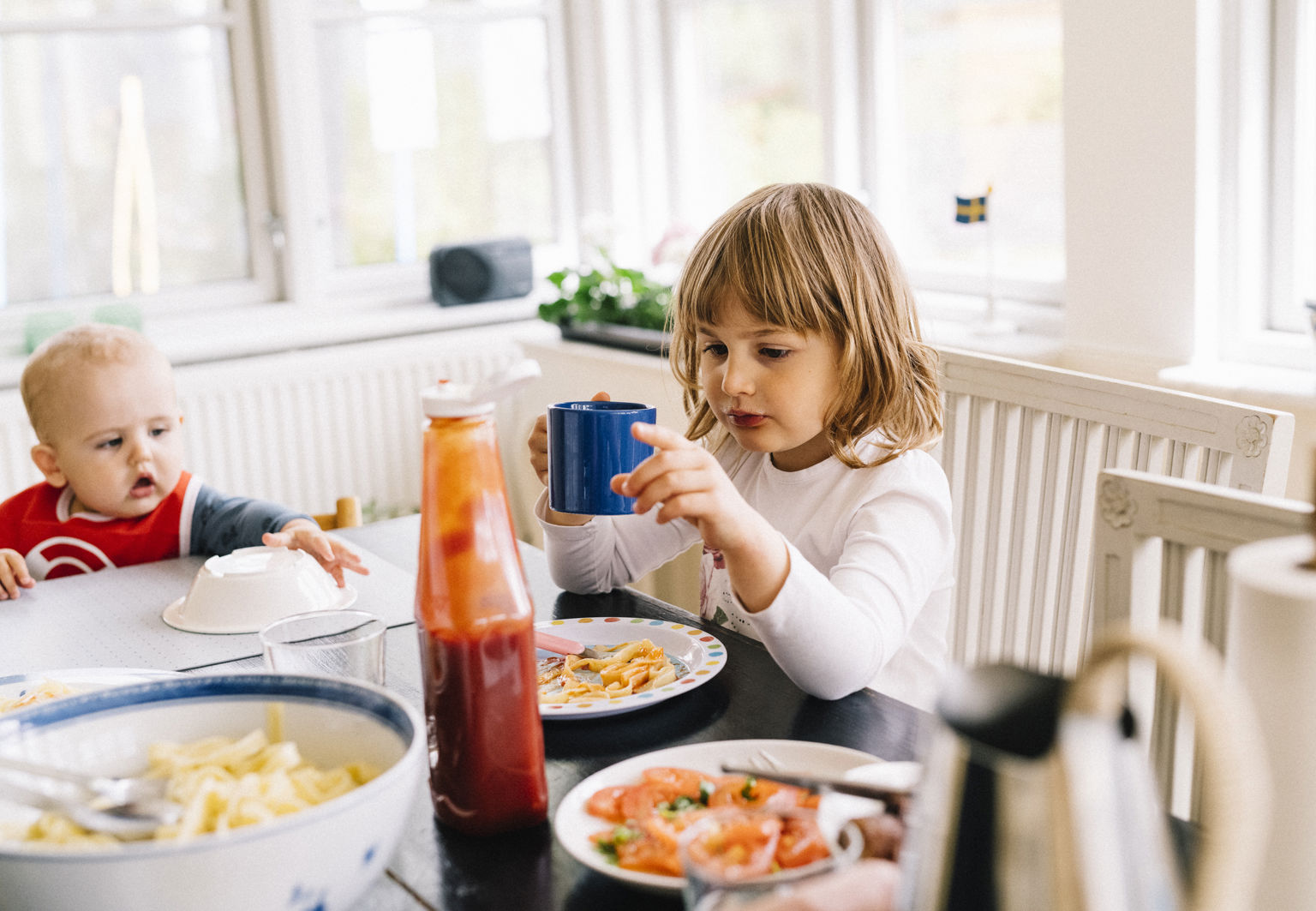 Två barn varav en bebis sitter vid ett matbord