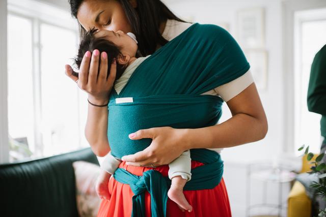 Mamma har en bebis i en bärsjal och myser kind mot kind