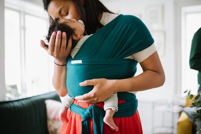 Mamma har en bebis i en bärsjal och myser kind mot kind