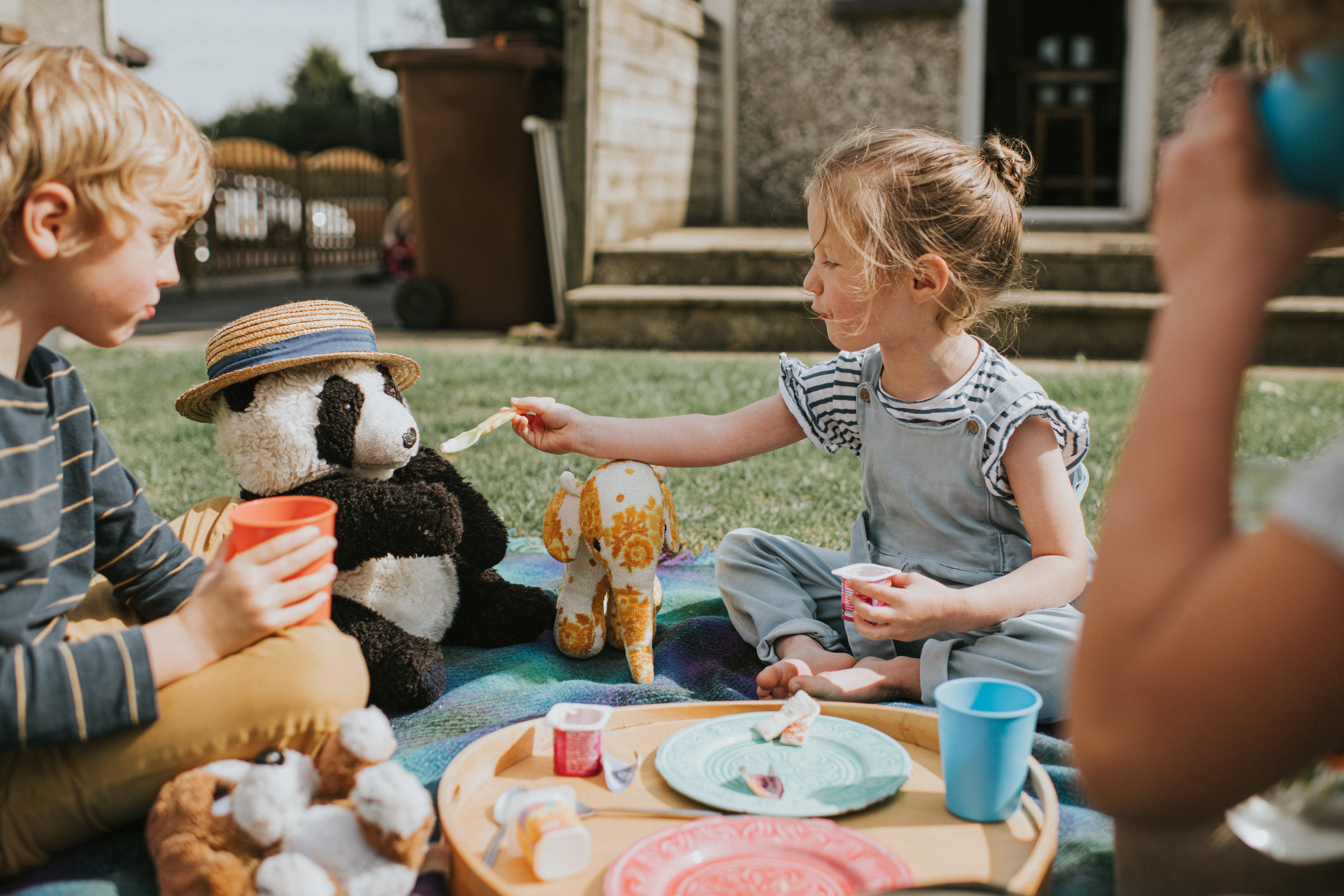 Barn har picknick och en flicka matar sitt gosedjur med sked