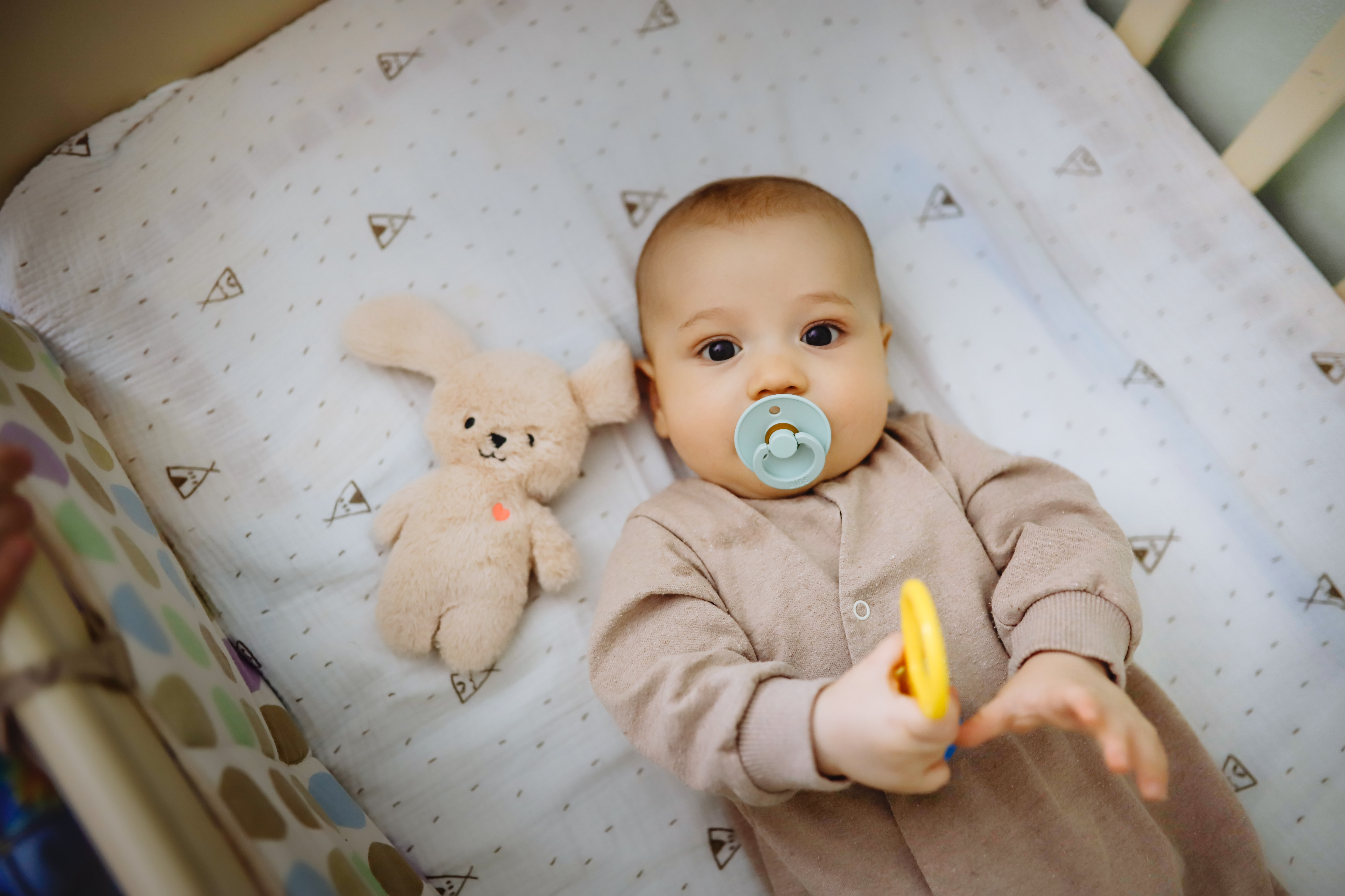 Bebis ligger vaken i en spjälsäng med napp i munnen