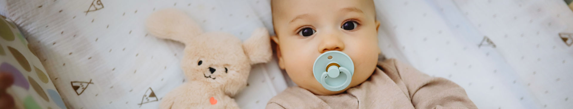 Bebis ligger vaken i en spjälsäng med napp i munnen
